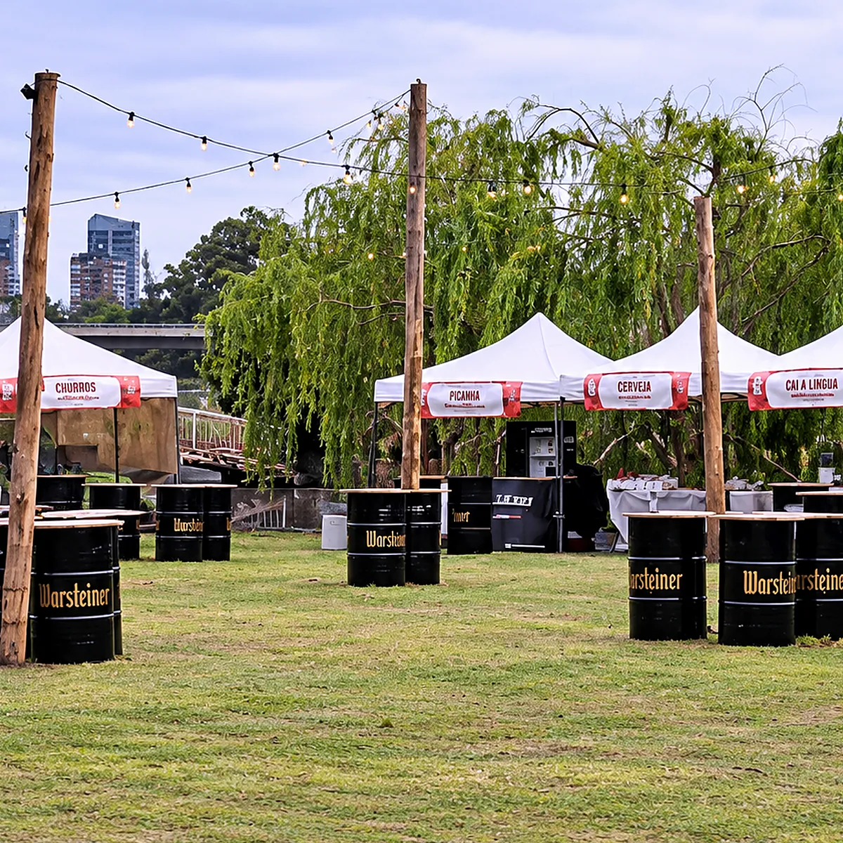 Guirnaldas de luces cálidas colgadas entre postes de madera sobre un festival con gazebos